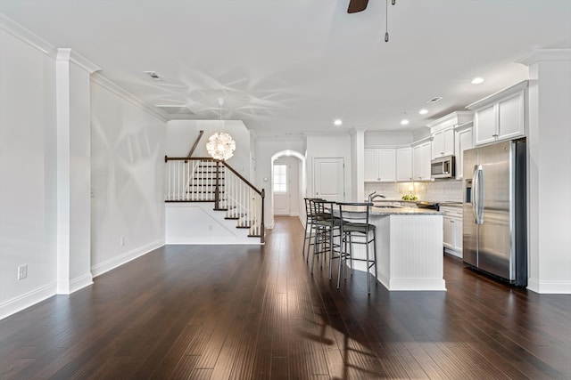 kitchen with appliances with stainless steel finishes, ceiling fan with notable chandelier, a kitchen island with sink, and dark hardwood / wood-style floors