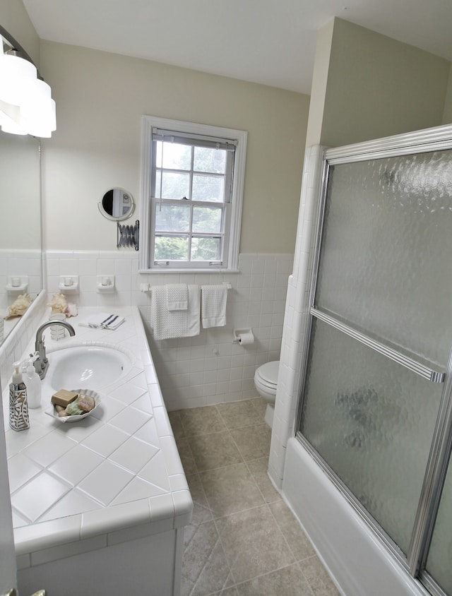 full bathroom with tile walls, bath / shower combo with glass door, vanity, and toilet