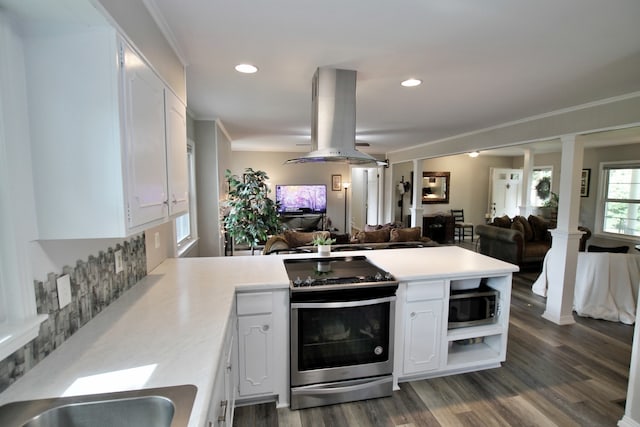 kitchen with kitchen peninsula, island range hood, white cabinetry, stainless steel appliances, and decorative columns