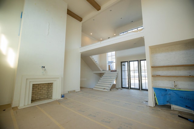 unfurnished living room featuring beamed ceiling and a high ceiling