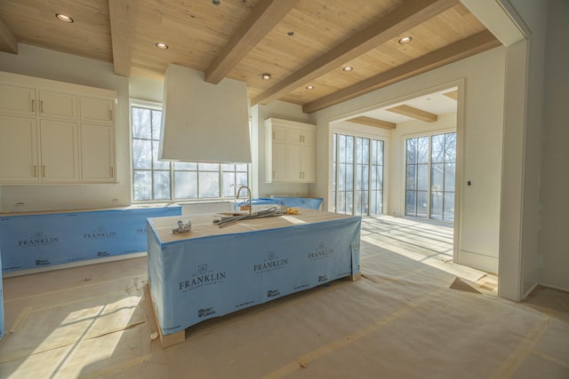 kitchen featuring a wealth of natural light, beam ceiling, a center island with sink, and white cabinets