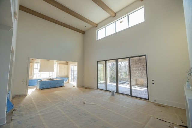 unfurnished living room featuring light colored carpet, beamed ceiling, and a high ceiling