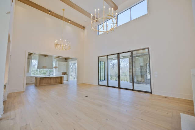 unfurnished living room with a chandelier, beam ceiling, a wealth of natural light, and light wood-style floors