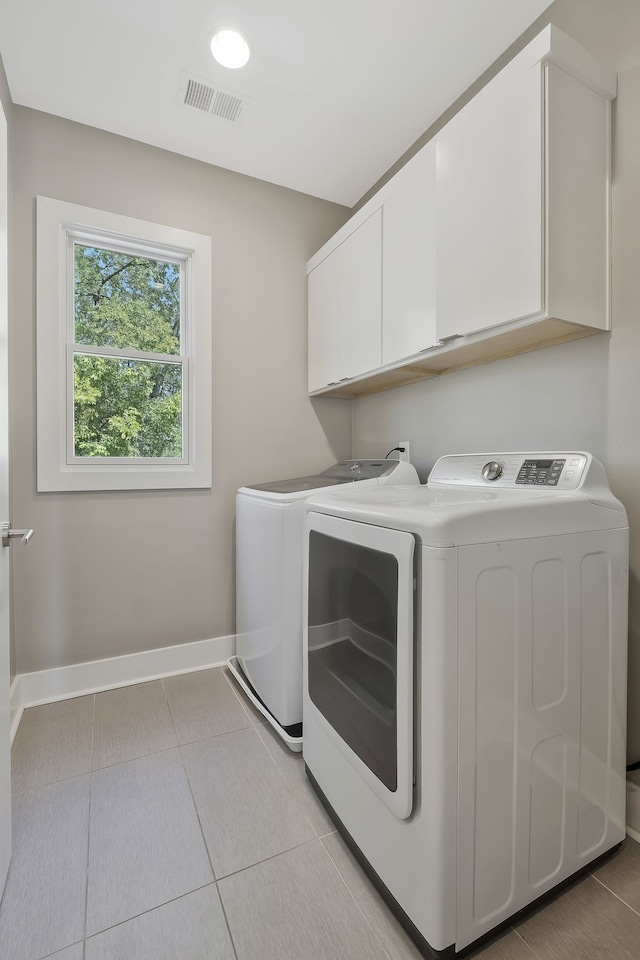 washroom featuring washing machine and dryer, light tile patterned floors, and cabinets