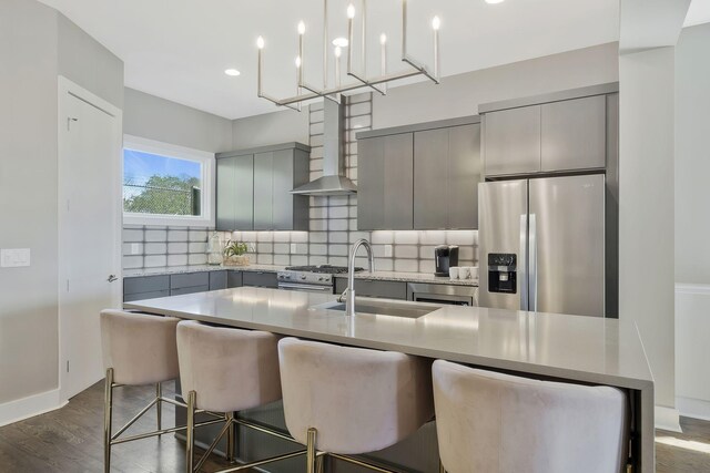 kitchen featuring an island with sink, gray cabinetry, wall chimney range hood, appliances with stainless steel finishes, and dark hardwood / wood-style floors