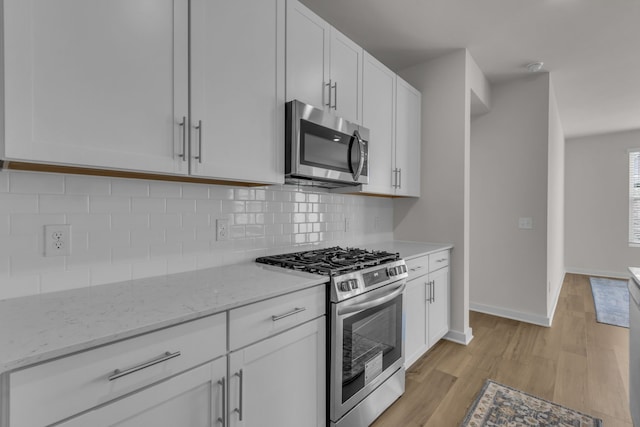 kitchen with decorative backsplash, white cabinetry, light stone counters, stainless steel appliances, and light hardwood / wood-style flooring