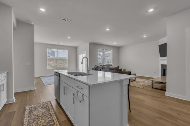 kitchen with light wood-type flooring, sink, white cabinets, a center island with sink, and stainless steel dishwasher