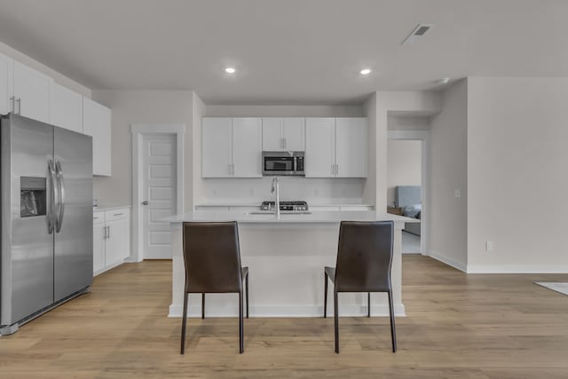 kitchen with white cabinets, a center island with sink, stainless steel appliances, a kitchen breakfast bar, and light hardwood / wood-style floors