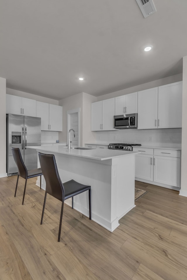 kitchen with white cabinets, a center island with sink, appliances with stainless steel finishes, and light wood-type flooring