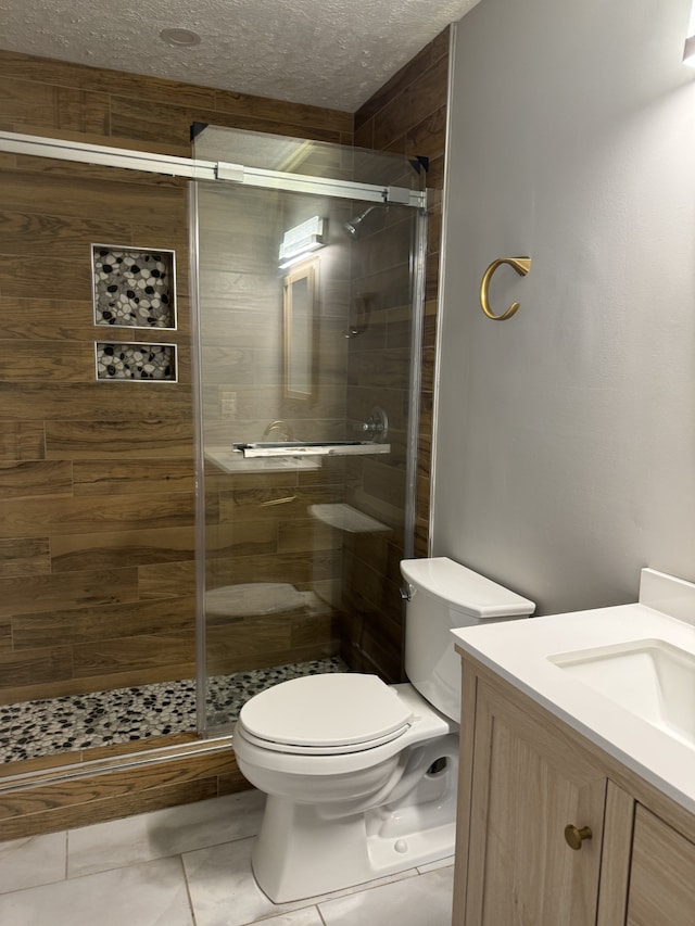 bathroom with vanity, a textured ceiling, tile patterned floors, toilet, and a shower with door