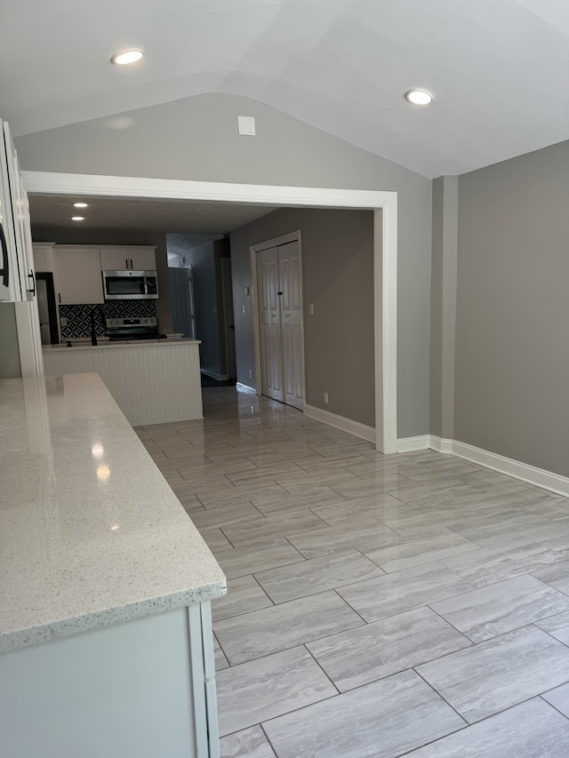 kitchen featuring light stone counters, white cabinets, lofted ceiling, tasteful backsplash, and appliances with stainless steel finishes