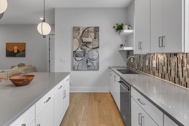 kitchen with white cabinetry, pendant lighting, light wood-type flooring, stainless steel dishwasher, and sink