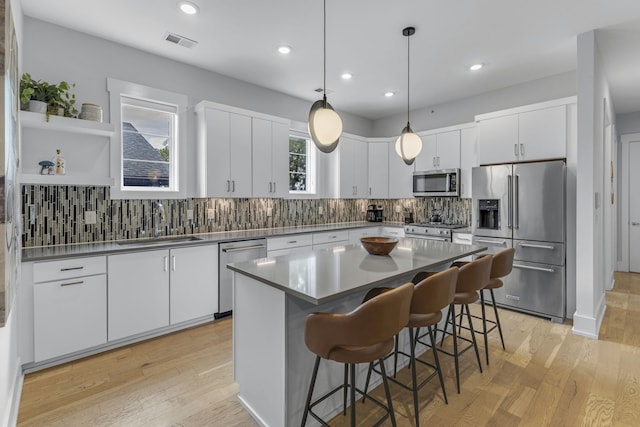 kitchen featuring stainless steel appliances, white cabinetry, and decorative light fixtures