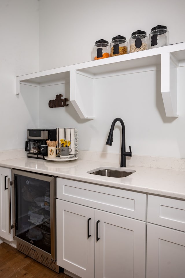 bar with light stone counters, dark hardwood / wood-style floors, sink, beverage cooler, and white cabinets