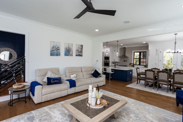 living room featuring ornamental molding, sink, ceiling fan with notable chandelier, and dark wood-type flooring