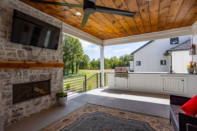 view of patio with ceiling fan, area for grilling, a grill, and an outdoor stone fireplace