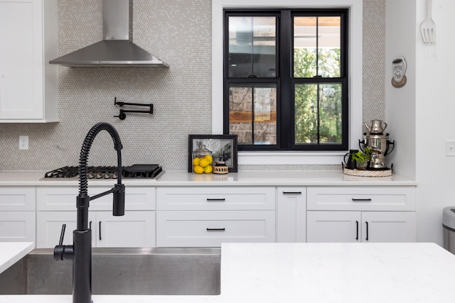 kitchen featuring stainless steel gas stovetop, wall chimney exhaust hood, tasteful backsplash, and white cabinets