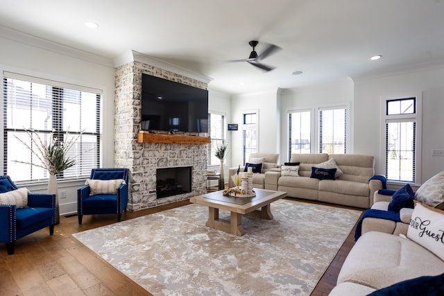 living room with a stone fireplace, a wealth of natural light, ceiling fan, and hardwood / wood-style flooring