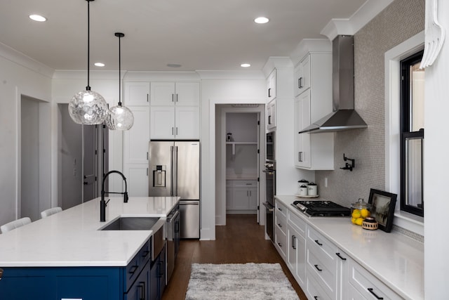 kitchen with a kitchen island with sink, white cabinets, wall chimney exhaust hood, appliances with stainless steel finishes, and blue cabinetry