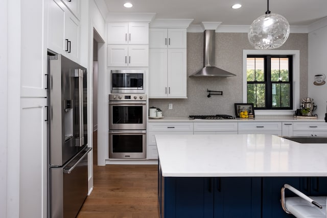 kitchen featuring stainless steel appliances, white cabinets, hanging light fixtures, and wall chimney range hood