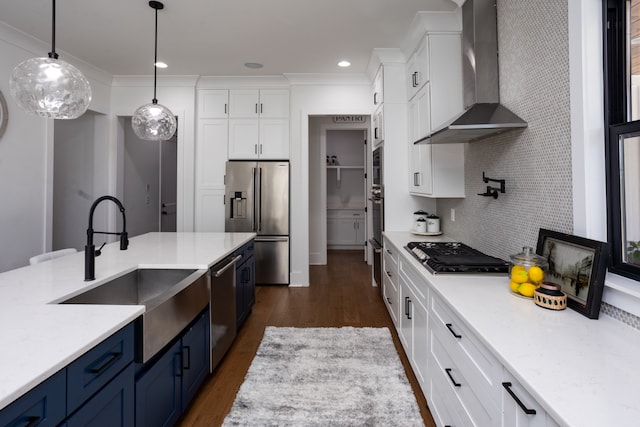 kitchen featuring white cabinetry, pendant lighting, blue cabinetry, stainless steel appliances, and wall chimney range hood