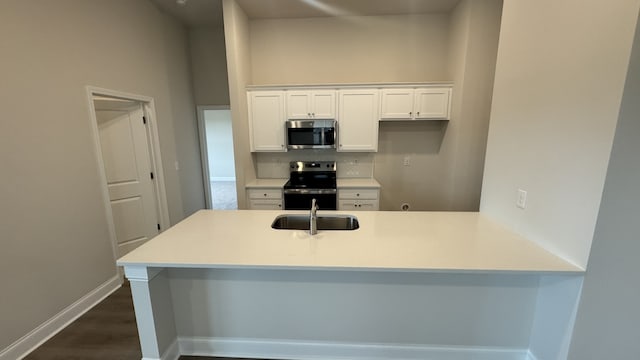 kitchen featuring kitchen peninsula, sink, backsplash, white cabinetry, and appliances with stainless steel finishes