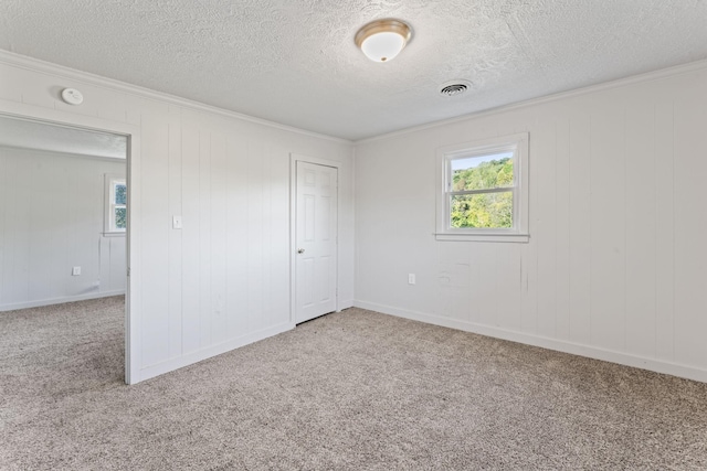 carpeted spare room featuring a textured ceiling, baseboards, visible vents, and ornamental molding