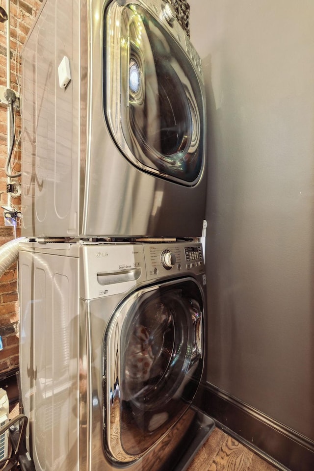laundry room with baseboards, stacked washer / dryer, laundry area, and brick wall