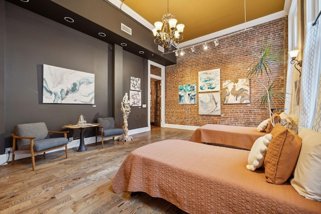 bedroom featuring a notable chandelier, wood finished floors, brick wall, baseboards, and ornamental molding