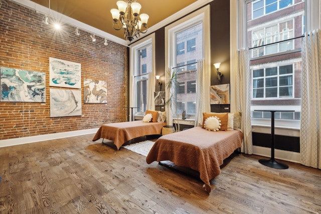 bedroom with wood finished floors, a chandelier, crown molding, and brick wall