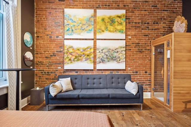 living area featuring baseboards, brick wall, and wood finished floors