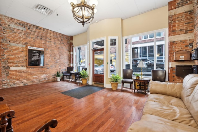 living room with visible vents, a chandelier, brick wall, and hardwood / wood-style flooring