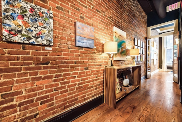 corridor with baseboards, brick wall, and wood finished floors