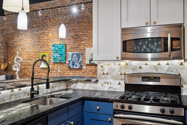 kitchen featuring blue cabinetry, decorative backsplash, hanging light fixtures, a sink, and appliances with stainless steel finishes