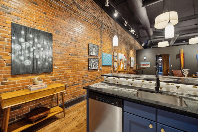 kitchen featuring track lighting, light wood finished floors, a sink, brick wall, and stainless steel dishwasher