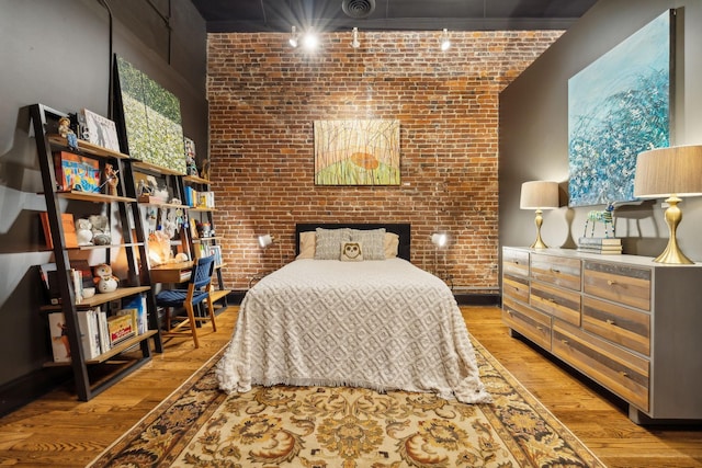 bedroom with visible vents, brick wall, and wood finished floors