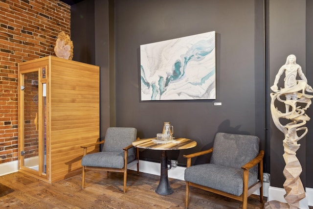 living area featuring baseboards, wood finished floors, and brick wall