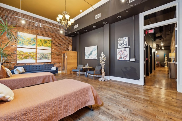 bedroom featuring a high ceiling, brick wall, visible vents, a notable chandelier, and wood finished floors
