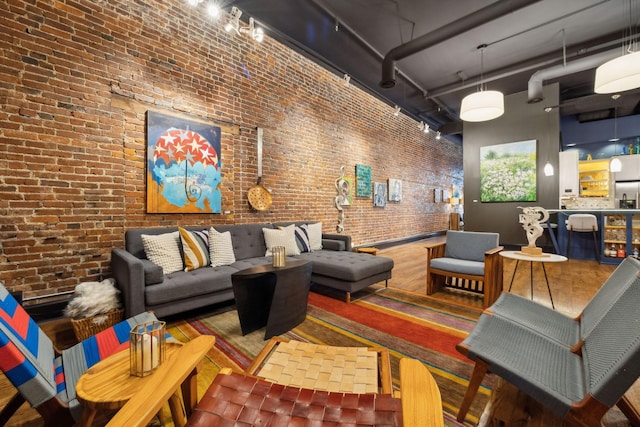 living area featuring rail lighting, a towering ceiling, and brick wall