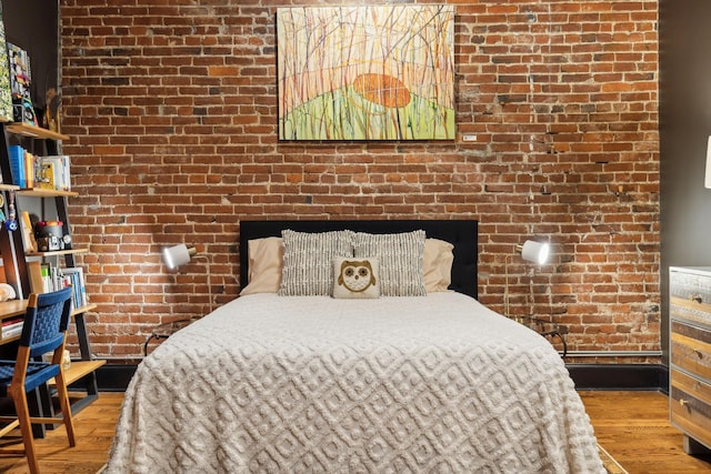 bedroom with wood finished floors and brick wall