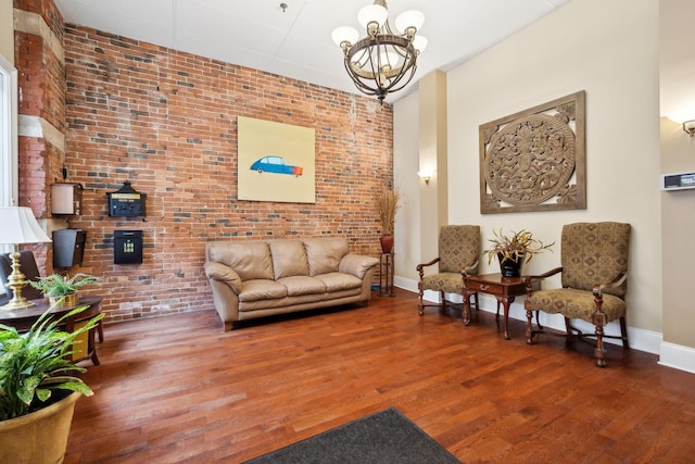 living area featuring baseboards, wood finished floors, a notable chandelier, and brick wall