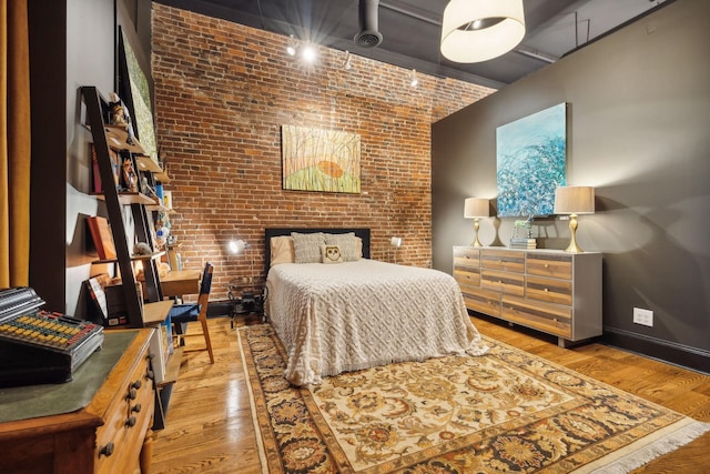 bedroom with baseboards, wood finished floors, and brick wall