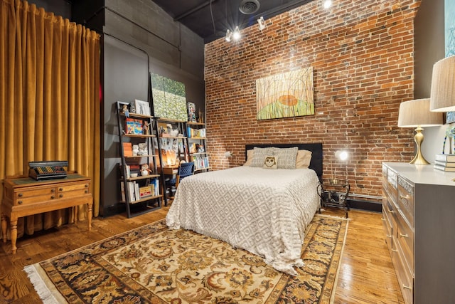 bedroom featuring a towering ceiling, light wood-type flooring, and brick wall