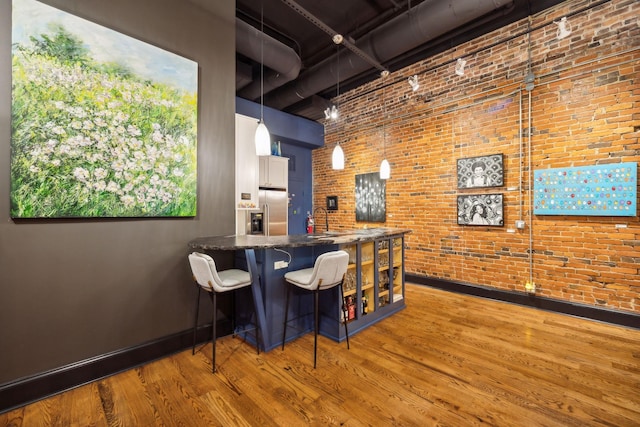 bar featuring baseboards, wood finished floors, brick wall, hanging light fixtures, and a high ceiling