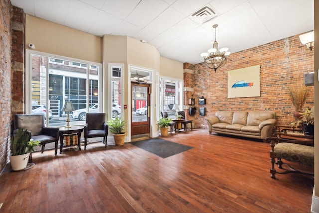 living area featuring hardwood / wood-style floors, visible vents, brick wall, and a chandelier