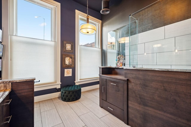 full bathroom with baseboards, a tile shower, and vanity