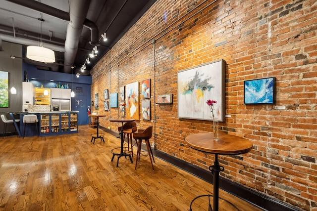 bar featuring a towering ceiling, wood finished floors, stainless steel refrigerator with ice dispenser, and brick wall