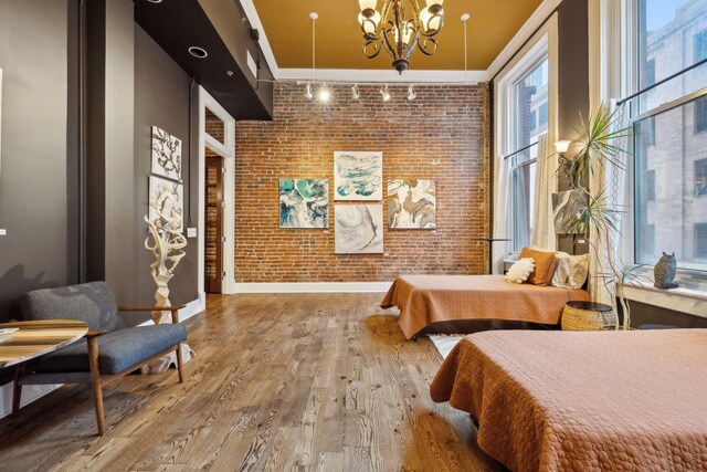 bedroom with a chandelier, crown molding, baseboards, wood finished floors, and brick wall