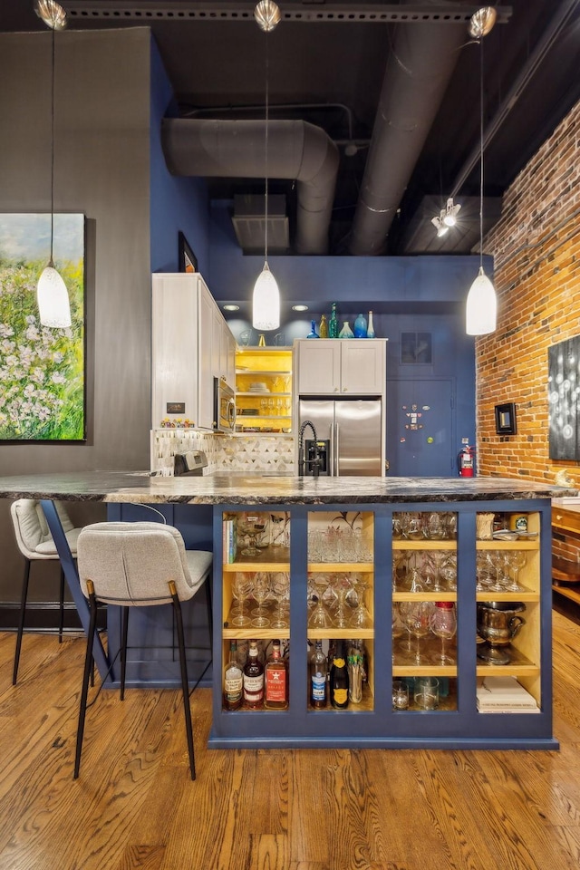 bar with tasteful backsplash, appliances with stainless steel finishes, light wood-type flooring, brick wall, and pendant lighting