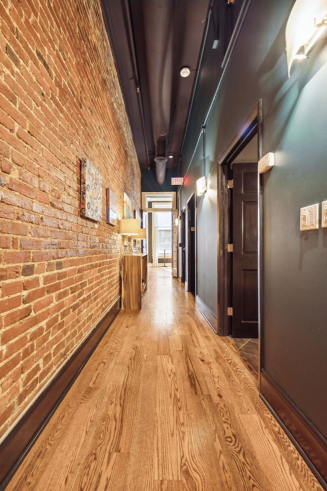 hallway featuring baseboards, brick wall, and wood finished floors